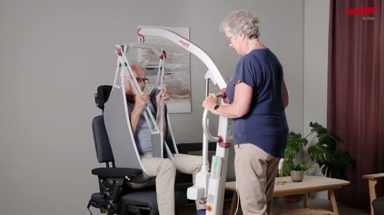 Elderly couple with woman lifting her husband from an armchair